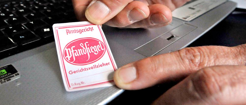 Ein Gerichtsvollzieher bringt an einem Laptop ein Pfandsiegel an.