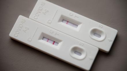 Ein positiver Corona-Schnelltest (l) liegt auf einem Tisch neben einem Corona-Schnelltest, der schwach eine positive Linie hat.