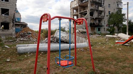Eine Kinderschaukel vor zerstörten Häusern in der Ukraine. 