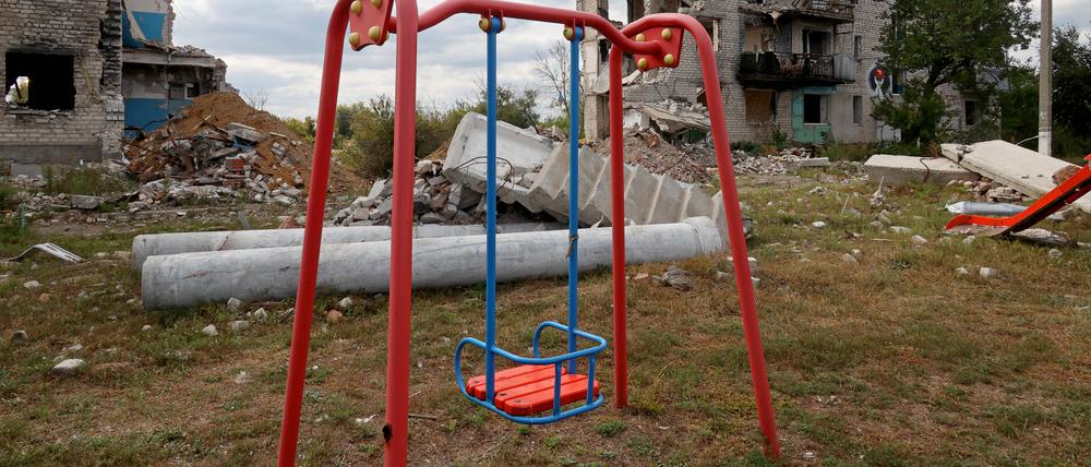 Eine Kinderschaukel vor zerstörten Häusern in der Ukraine.