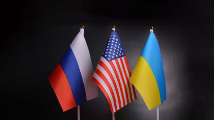 Die Flaggen von Russland, USA und der Ukraine stehen vor schwarzem Hintergrund. Symbolbild für 3er-Gipfel.