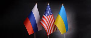 Die Flaggen von Russland, USA und der Ukraine stehen vor schwarzem Hintergrund. Symbolbild für 3er-Gipfel.
