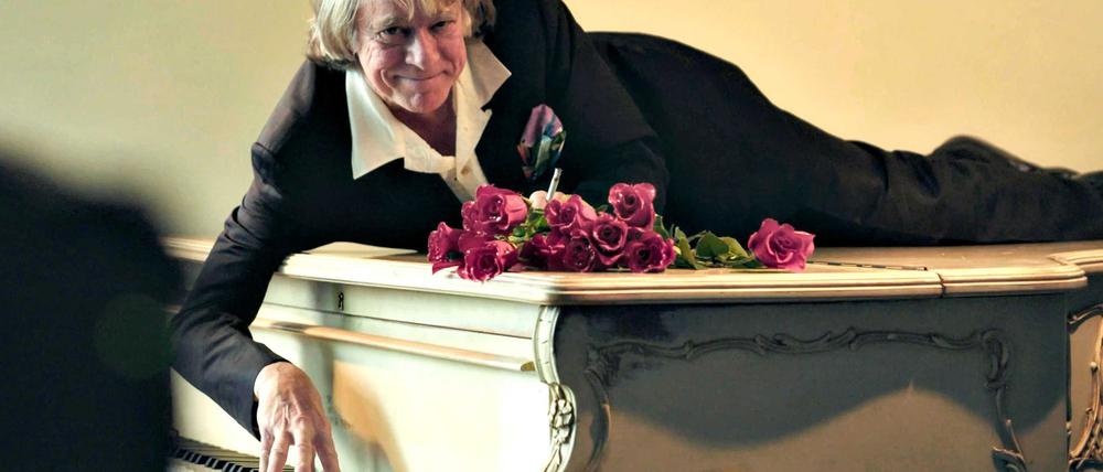 Helge Schneider liegt auf einem Klavier in einer Szene des Films „Helge Schneider - The Klimperclown“, der nun in der Mediathek zu sehen ist und am Mittwoch, 20.8., im Ersten gezeigt wird.