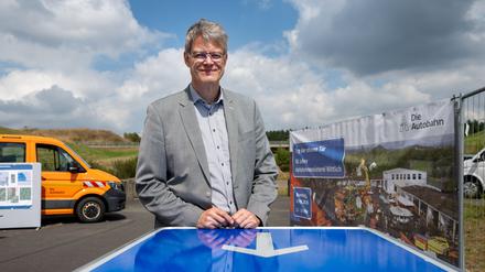 Bundesverkehrsminister Patrick Schnieder (CDU) steht an der Autobahn A1-Lückenanschlussstelle Kelberg an einem Tisch, dessen Platte einst ein Autobahnschild war.