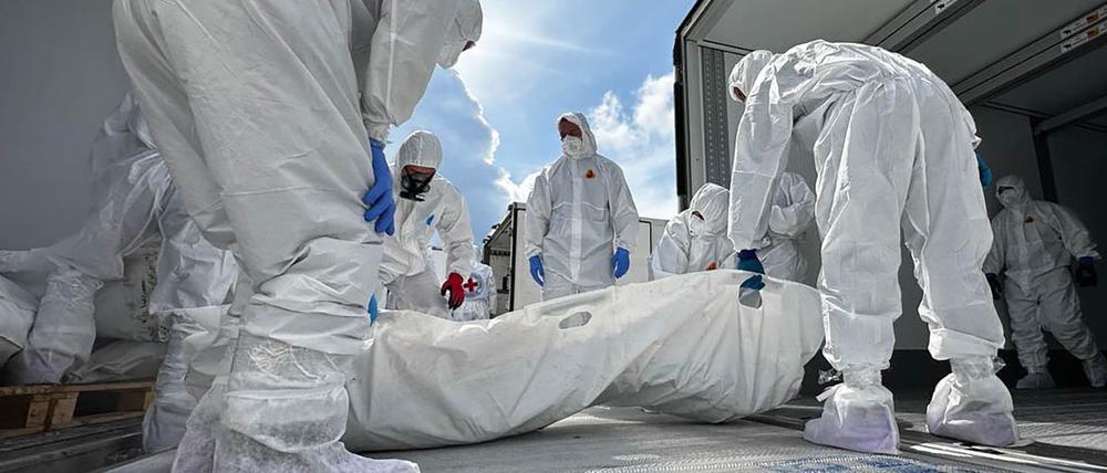 In weiße Schutzanzüge gekleidete Personen verladen Leichen in dafür bereitstehende Lastwagen im Rahmen des Austauschs zwischen Kiew und Moskau.