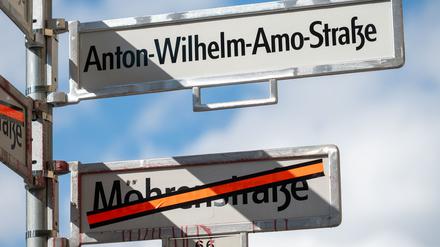 Ein Schild mit der Aufschrift „Anton-Wilhelm-Amo-Straße“ hängt über einem Schild, auf dem der Name „Mohrenstraße“ durchgestrichen ist. 
