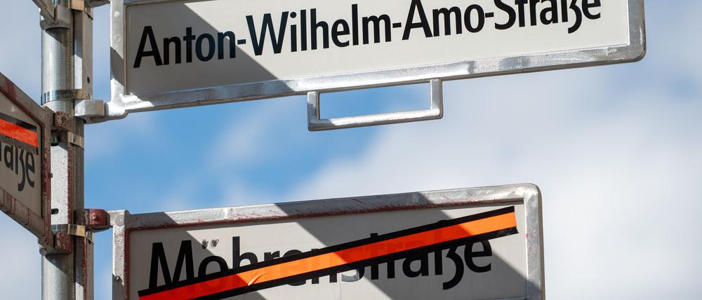 Ein Schild mit der Aufschrift „Anton-Wilhelm-Amo-Straße“ hängt über einem Schild, auf dem der Name „Mohrenstraße“ durchgestrichen ist.