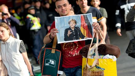 Ein Flüchtling, der kurz zuvor mit einem Zug angekommen ist, läuft auf dem Hauptbahnhof über den Bahnsteig und hält dabei ein Foto von Angela Merkel in den Händen.