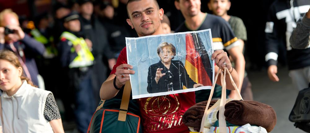 Ein Flüchtling, der kurz zuvor mit einem Zug angekommen ist, läuft auf dem Hauptbahnhof über den Bahnsteig und hält dabei ein Foto von Angela Merkel in den Händen.