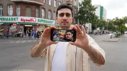 Anas Modamani steht auf der Sonnenallee in Berlin. Der Syrer kam 2015 als Flüchtling nach Deutschland. Er zeigt auf seinem Handy ein Selfie mit der damaligen Bundeskanzlerin Angela Merkel. 
