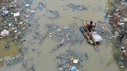 Bangladesch: Ein Vater rudert mit seinem Sohn auf einem handgefertigten Floß und sucht im mit Plastikmüll gefüllten Kanal von Kazir Bazar in Sylhet nach Recyclingprodukten aus Plastik. 