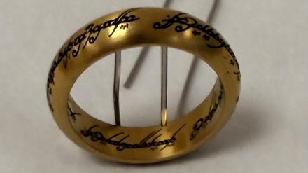 Ein goldener Metallring mit Worten in Elbenschrift steht an eine Büroklammer gelehnt. In Hamburg hat jemand einen Ring gefunden, der dem aus dem Filmepos «Herr der Ringe» nachempfunden ist. 