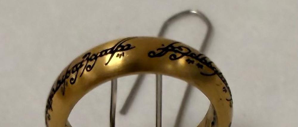 Ein goldener Metallring mit Worten in Elbenschrift steht an eine Büroklammer gelehnt. In Hamburg hat jemand einen Ring gefunden, der dem aus dem Filmepos «Herr der Ringe» nachempfunden ist. 