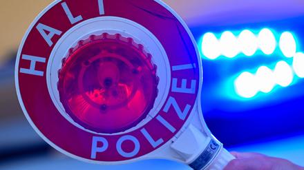 Eine Kelle der Polizei mit der Aufschrift Halt Polizei vor einem Blaulicht eines Polizeifahrzeuges. (Symbolbild)