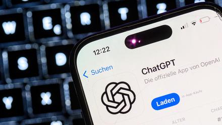 Ein Smartphone mit der App des KI-Chatbots ChatGPT ist vor dem Logo des US-Softwareunternehmens OpenAI zu sehen.