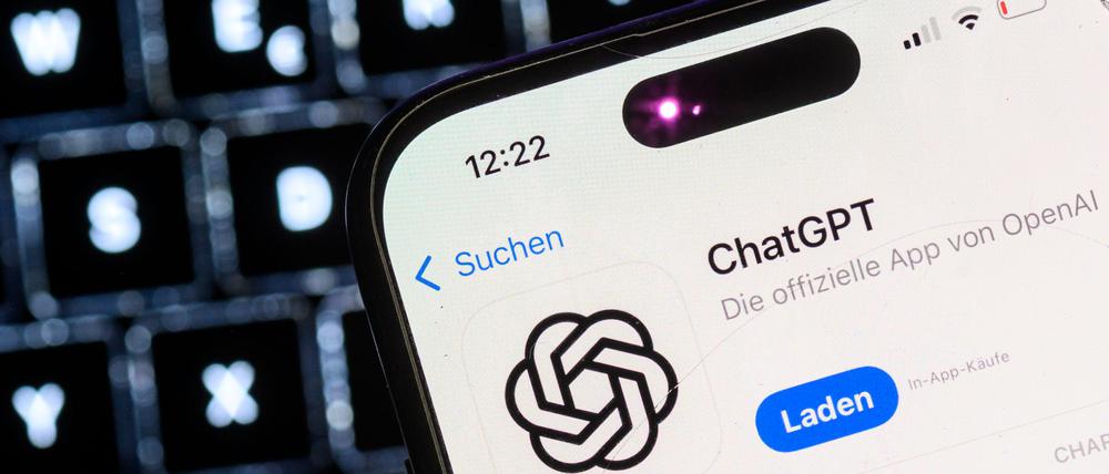 Ein Smartphone mit der App des KI-Chatbots ChatGPT ist vor dem Logo des US-Softwareunternehmens OpenAI zu sehen.