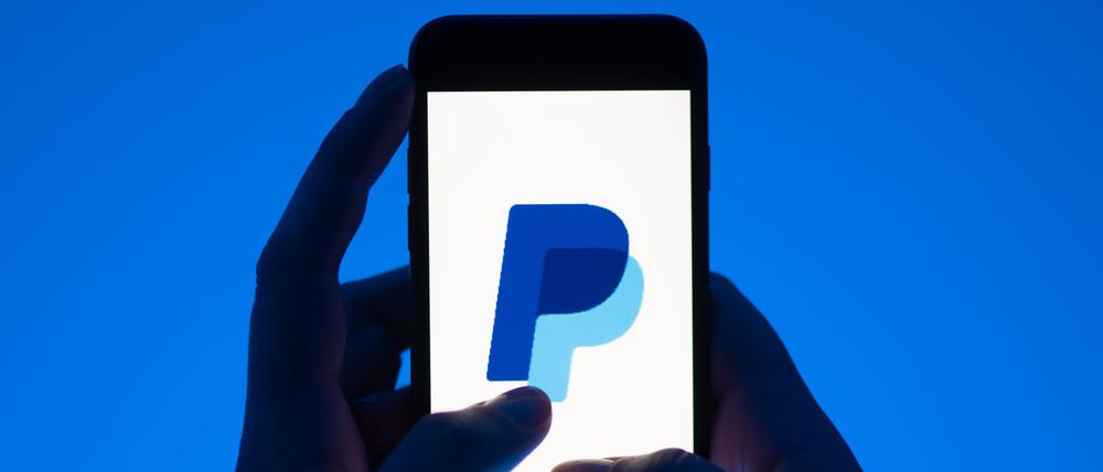 Eine Frau hält ein Smartphone mit dem Logo des Bezahldienstes Paypal.