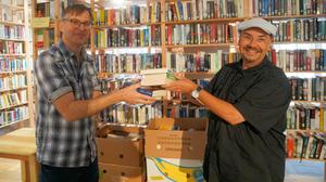 Jordan Wegberg (rechts) übergibt eine Bücherspende an den Leiter der Berliner "Vita-Bücherbörse", Lars Friedrich.