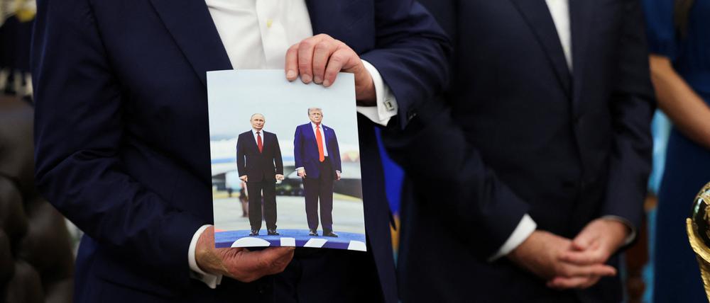 U.S. President Donald Trump holds an image of him and Russian President Vladimir Putin from their meeting in Alaska, as President Trump makes an announcement on the 2026 FIFA World Cup, in the Oval Office at the White House in Washington, D.C., U.S., August 22, 2025. REUTERS/Jonathan Ernst