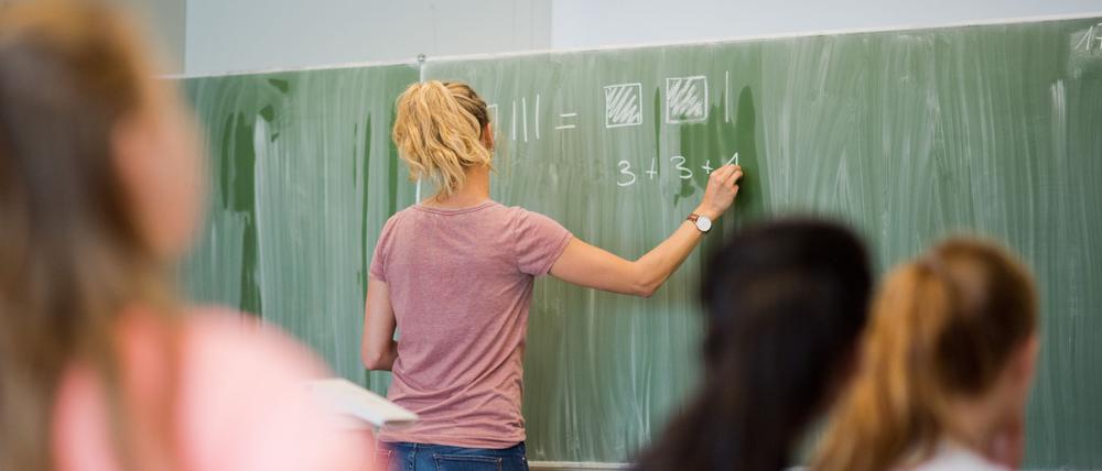 Eine junge Lehrerin schreibt an einer Schultafel.