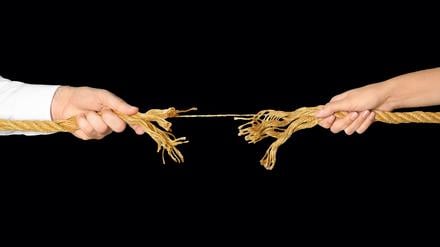Man and woman pulling frayed rope at breaking point on gray background 