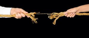 Man and woman pulling frayed rope at breaking point on gray background 