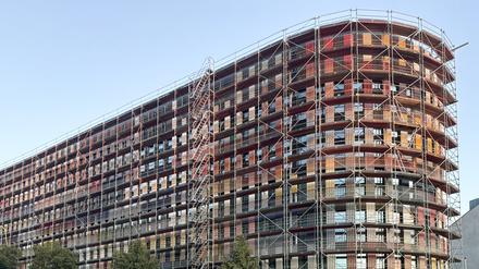 Ein gerundetes Gebäude mit sieben Stockwerken, noch mit einem Gerüst. Die Fassade ist bunt in Regenbogenfarben.
