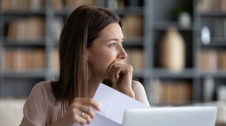 Eine Frau blickt nachdenklich zur Seite. In der Hand hält sie einen Brief.