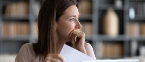 Eine Frau blickt nachdenklich zur Seite. In der Hand hält sie einen Brief.