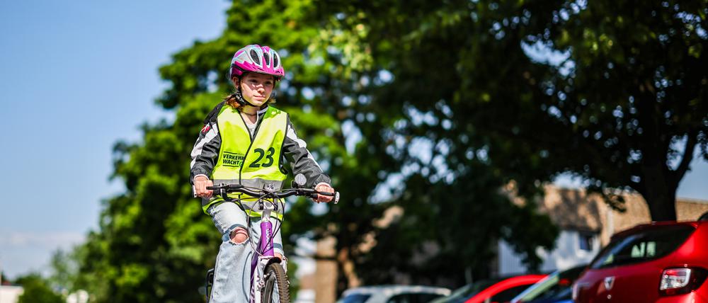 Eine Grundschülerin fährt auf ihrem Fahrrad bei einer Grundschule vor parkenden Autos entlang.