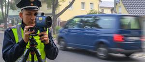 Ein Polizeibeamter überwacht mit einem Lasermessgerät die Geschwindigkeit von Straßenverkehrsteilnehmern vor einer Schule. 