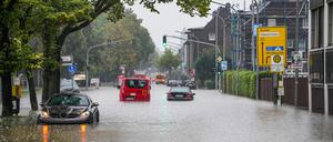 Autos fahren bei starkem Regen durch eine überflutete Straße.
