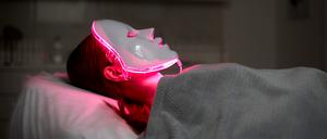 Eine Frau lässt sich mit einer LED-Maske mit rotem Licht behandeln. (Symbolbild)