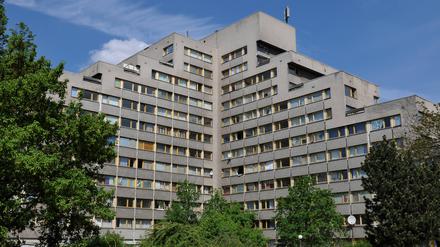 Ein großes Wohngebäude mit  mehreren Flügeln mit abgestuften Stockwerken, umrandet von Bäumen.  