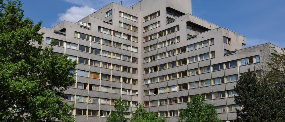 Ein großes Wohngebäude mit  mehreren Flügeln mit abgestuften Stockwerken, umrandet von Bäumen.  