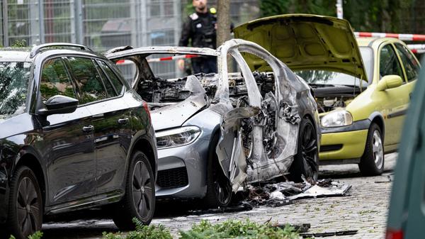 Ein ausgebranntes Auto und weitere zum Teil beschädigte Fahrzeuge stehen an einem Straßenrand. Bei der Explosion eines Sprengsatzes in oder an einem Auto in Berlin-Schöneberg ist ein 22-jähriger Mann schwer verletzt worden.