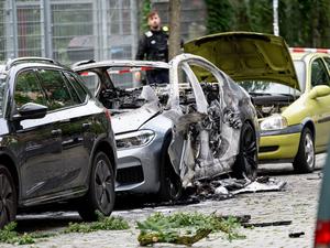 Ein ausgebranntes Auto und weitere zum Teil beschädigte Fahrzeuge stehen an einem Straßenrand. Bei der Explosion eines Sprengsatzes in oder an einem Auto in Berlin-Schöneberg ist ein 22-jähriger Mann schwer verletzt worden.