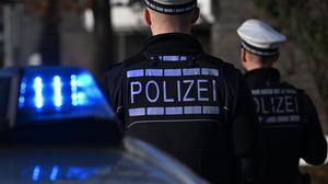Das Logo der Polizei auf der Dienstkleidung von Polizisten die vor einem Blaulicht stehen (gestellte Szene).