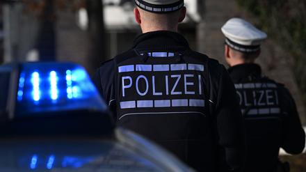 Das Logo der Polizei auf der Dienstkleidung von Polizisten die vor einem Blaulicht stehen (gestellte Szene).