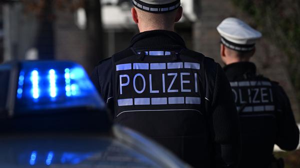 Das Logo der Polizei auf der Dienstkleidung von Polizisten die vor einem Blaulicht stehen (gestellte Szene).