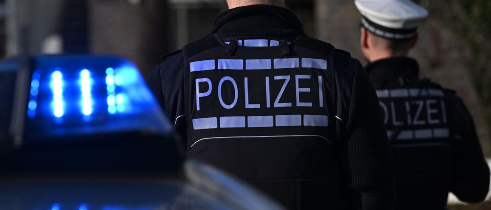 Das Logo der Polizei auf der Dienstkleidung von Polizisten die vor einem Blaulicht stehen (gestellte Szene).