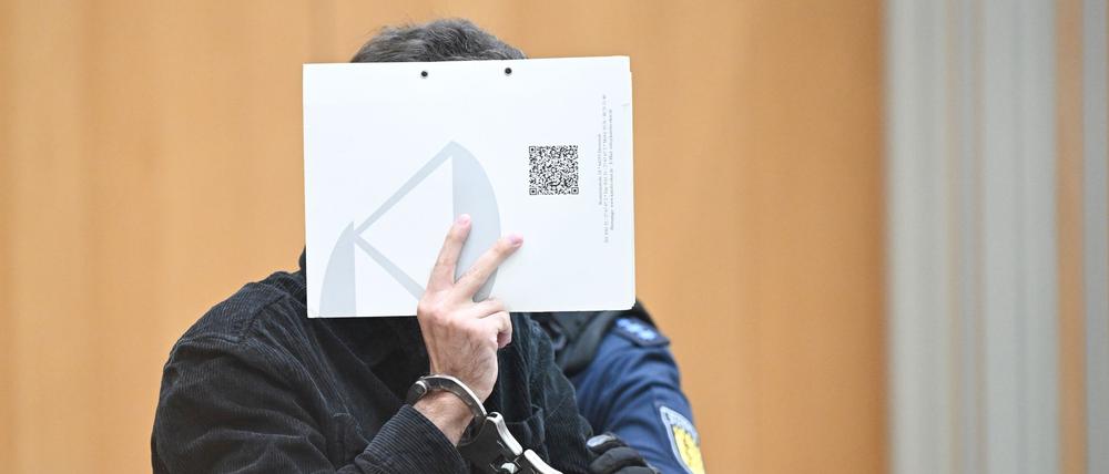 Stuttgart: Der Angeklagte in einem Staatsschutzverfahren steht zu Beginn eines Verhandlungstages mit einem Aktenordner vor dem Gesicht im Gerichtssaal. 