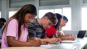 African american teen high school student writing, doing homework in class with multiracial classmates. Group of college students taking notes in class. Education.