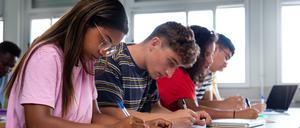 African american teen high school student writing, doing homework in class with multiracial classmates. Group of college students taking notes in class. Education.