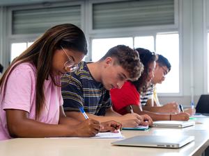 African american teen high school student writing, doing homework in class with multiracial classmates. Group of college students taking notes in class. Education.