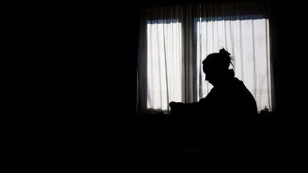 Die Silhouette einer Frau zeichnet sich vor einer hellen Fensterfront ab (gestellte Szene). 