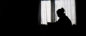 Die Silhouette einer Frau zeichnet sich vor einer hellen Fensterfront ab (gestellte Szene). 