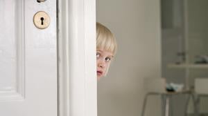 Ein scheues Kind versteckt sich hinter einer Tür.