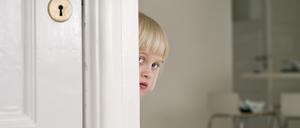 Ein scheues Kind versteckt sich hinter einer Tür.