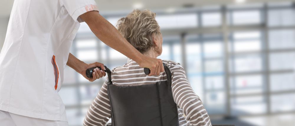 Eine alte Frau wird von Klinikpersonal in einem Rollstuhl geschoben.